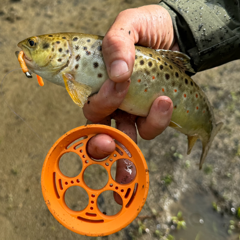 Orange GoReel hand reel held with a trout beside the river