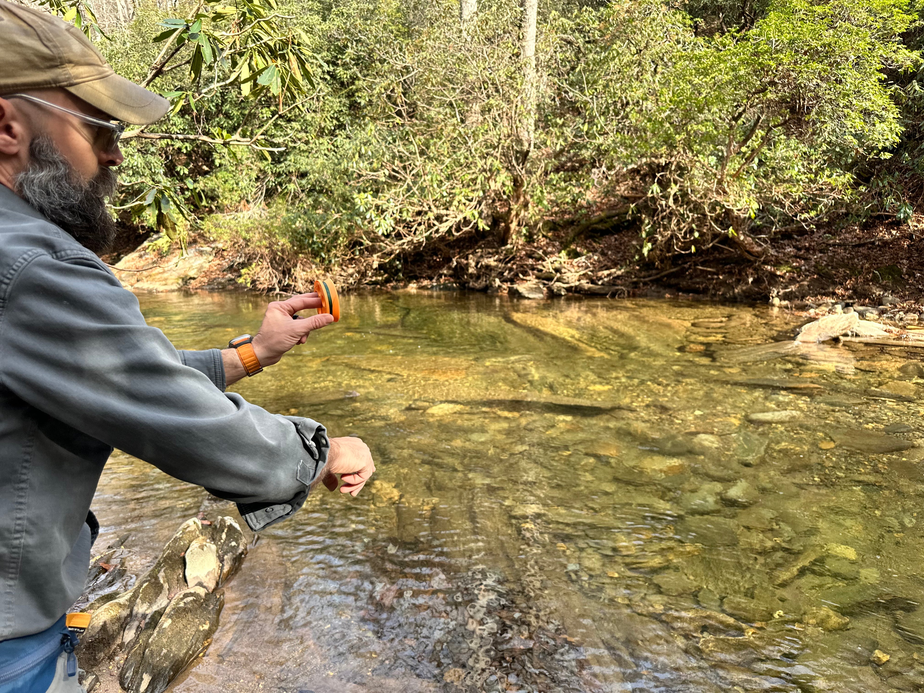 Man fishing by a river with trees and rocks in the background
